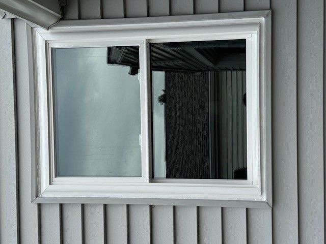 White sliding window in gray siding, reflecting the surroundings.