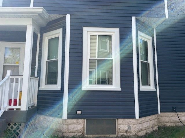 Blue house exterior with white trim, three windows, and a small basement window.