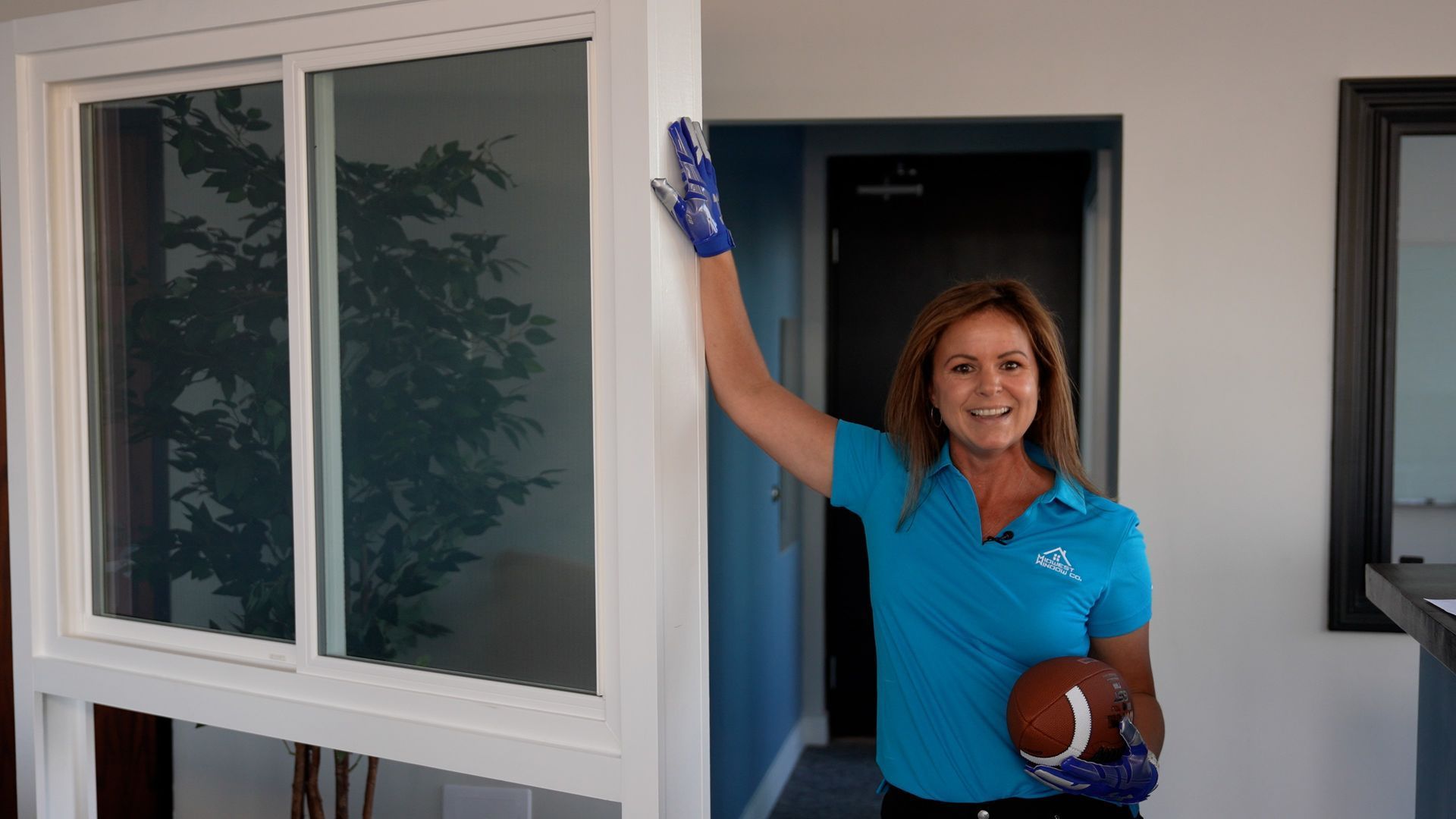 Woman in blue shirt holding football, standing next to window, arm raised. Woman in blue shirt holding football, standing next to window, arm raised.