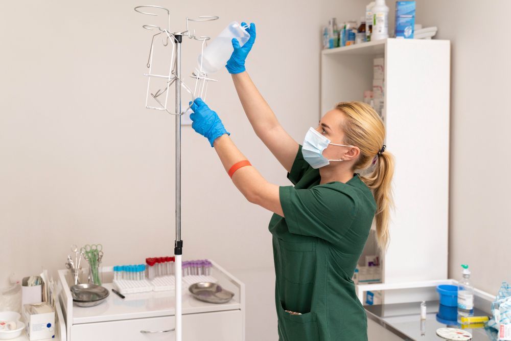 A nurse wearing a mask and gloves is preparing an iv in a hospital room.