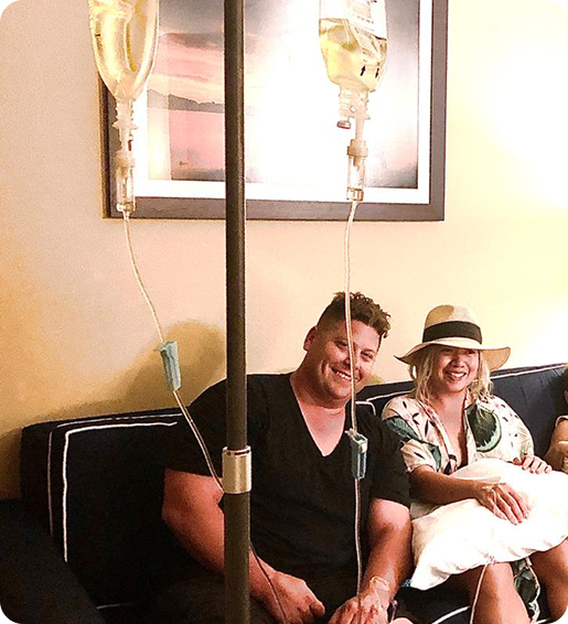 A man and a woman are sitting on a couch with iv drips attached to them.