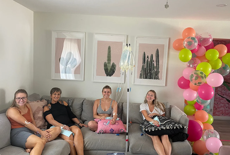 A group of women are sitting on a couch with balloons in the background.