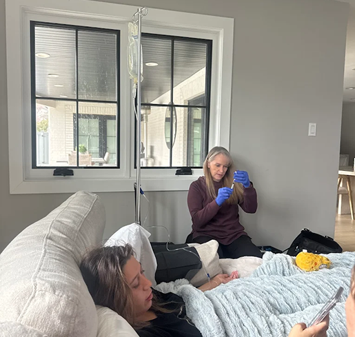 A woman is sitting on a couch next to a woman laying on a bed.