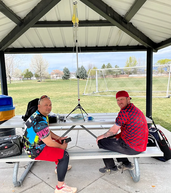 Two men are sitting at a picnic table under a gazebo.
