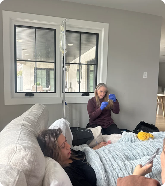 A woman is sitting on a couch next to a woman laying on a bed.