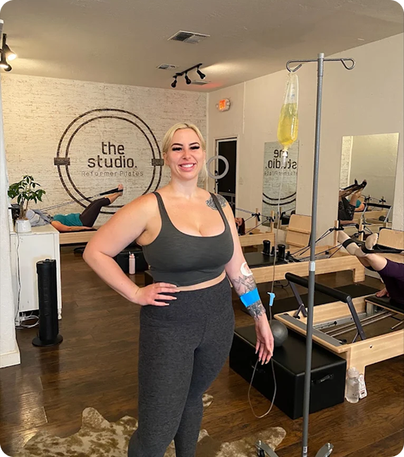 A woman is standing in a pilates studio with an iv in her arm.