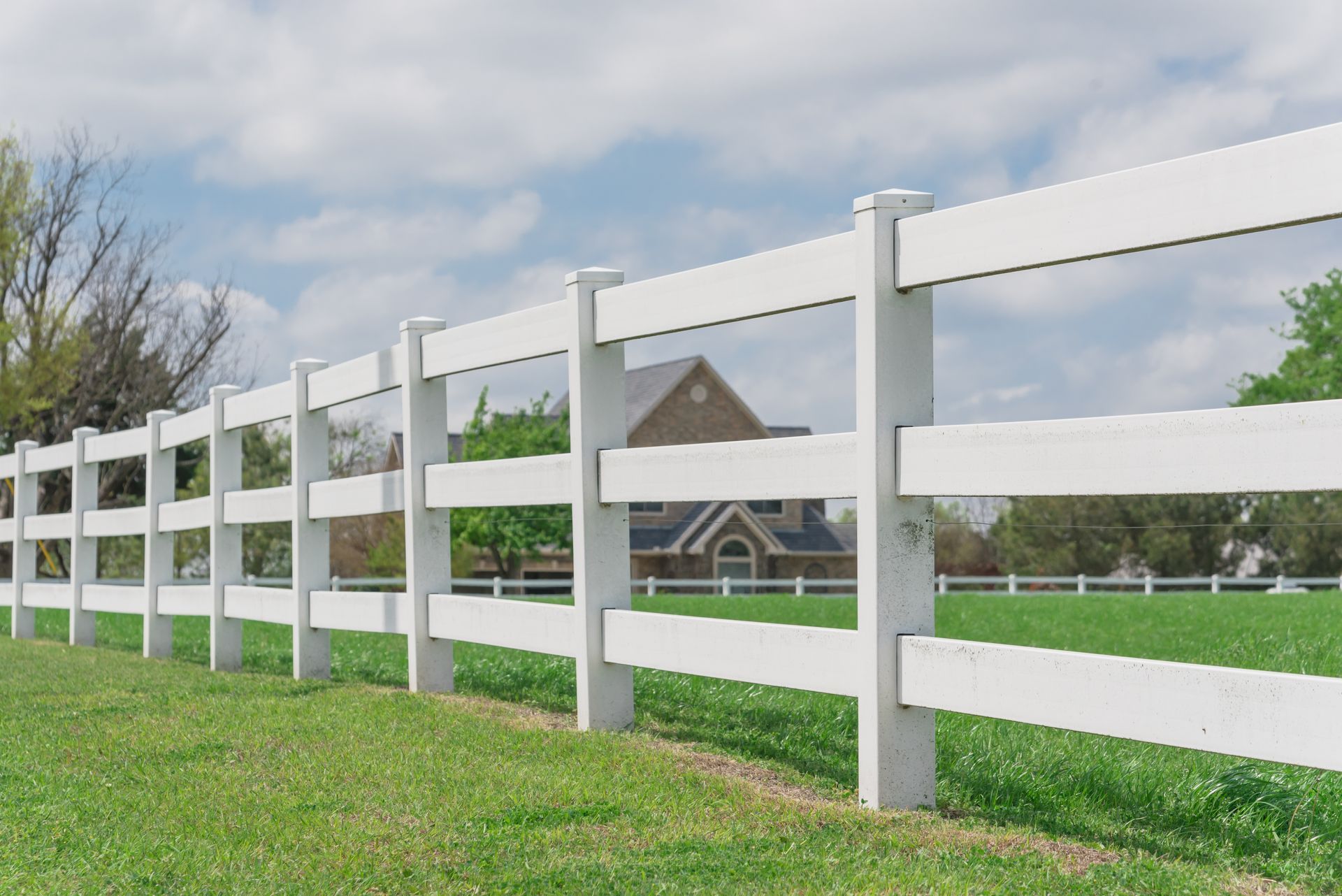 Blurred farmhouse ranch in the distance, framed by a long white fence with shallow depth of field.