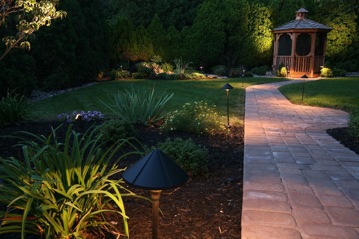 Vibrantly illuminated garden pathway at dusk, with warm landscape lighting accentuating the lush greenery and delicate flowers.