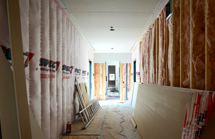 A hallway with insulation installed between the studs. Drywall sheets are stacked and lying against 