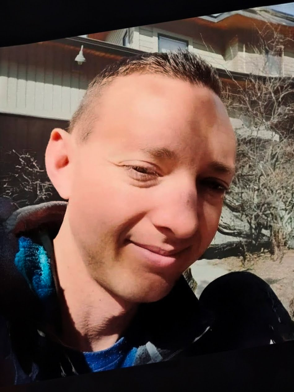 Man smiling in front of a white door wearing a black polo shirt.