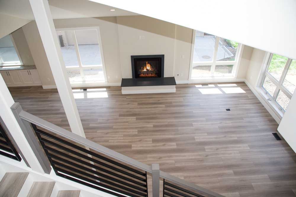 View from staircase of living room with fireplace, large windows, and light wood-look flooring.