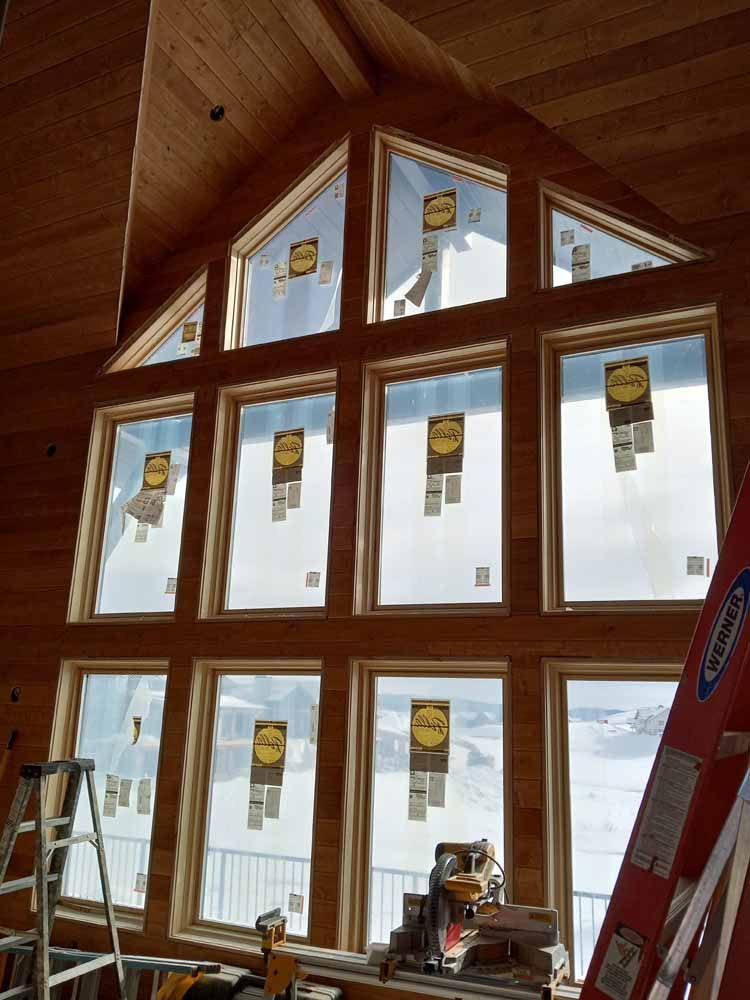 Large wood-framed windows with protective paper in a wooden house, snowy exterior visible.