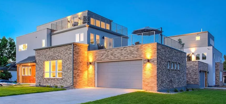 Modern multi-story house with stone facade, garage, and rooftop patio under a twilight sky.