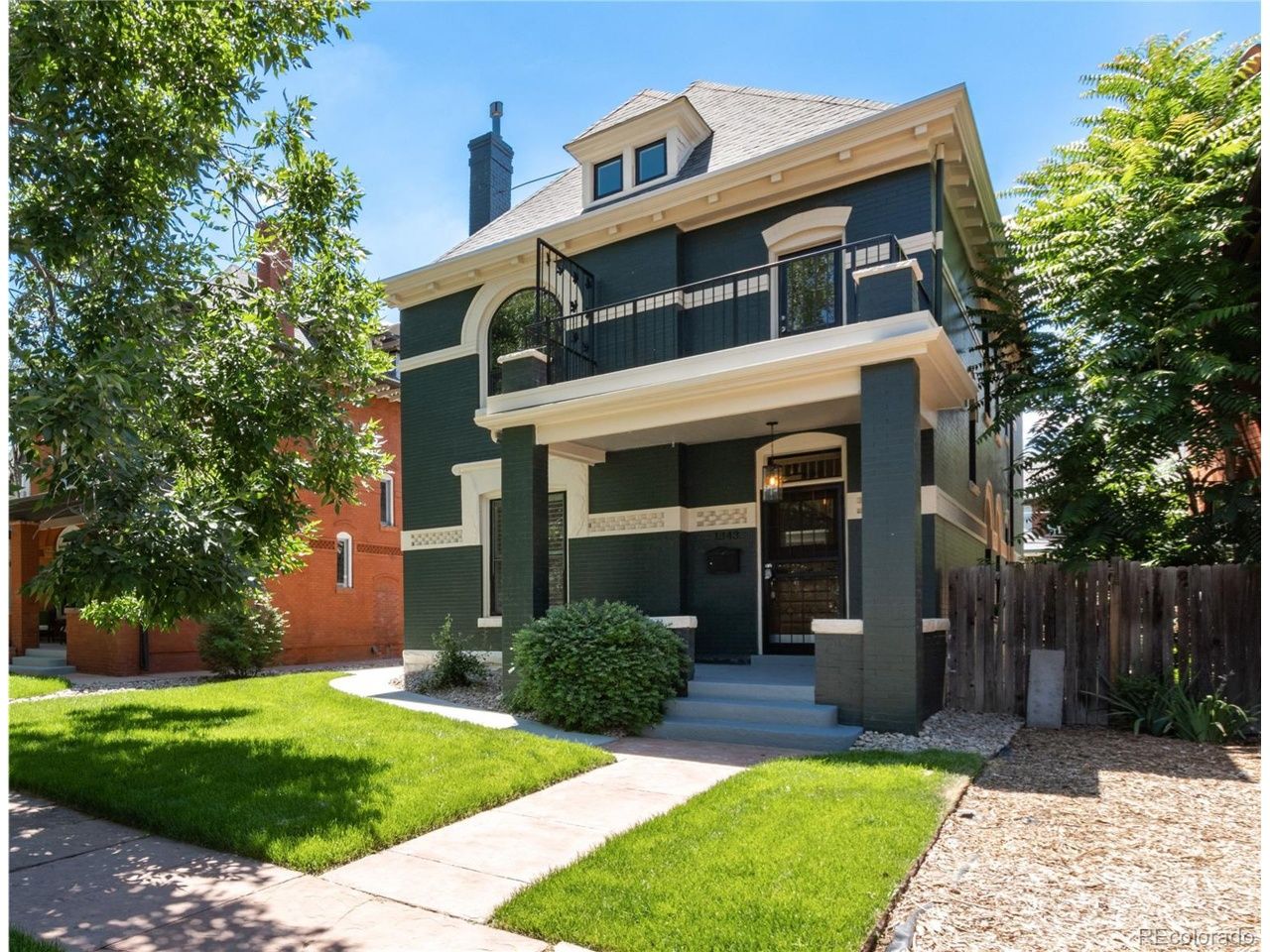 Dark green two-story house with white trim, front porch, and small yard, surrounded by trees and grass.