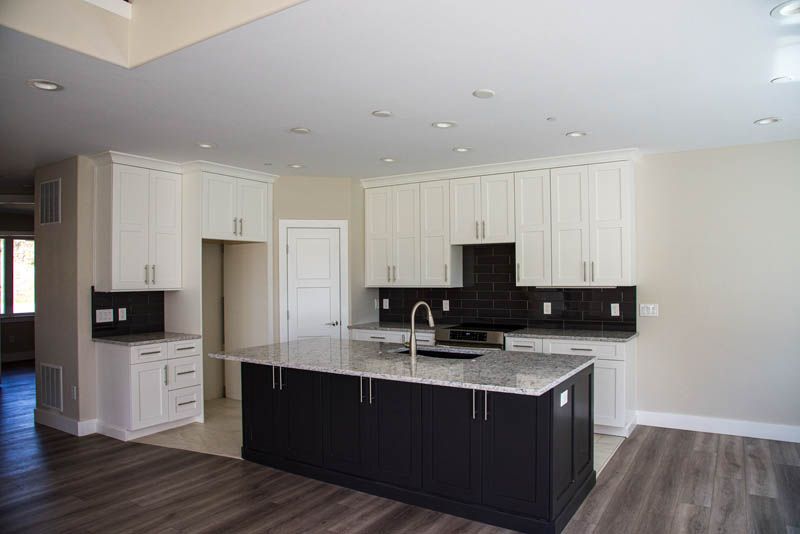 Modern kitchen with white and black cabinets, island with granite countertop.