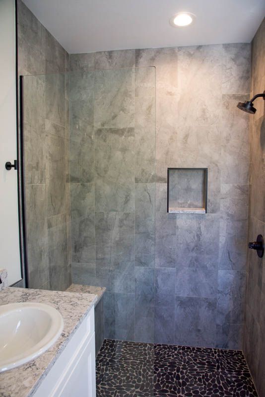 Shower with gray stone tile walls, a pebble floor, and a built-in shelf. A white sink is visible on the left.