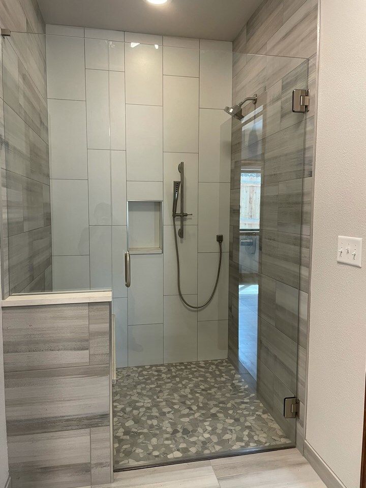 Modern shower with pebble floor, glass doors, and light gray tile walls.