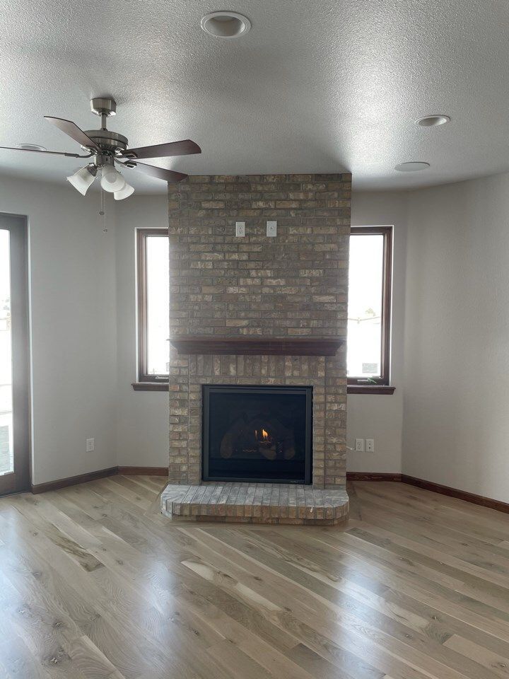 Living room with brick fireplace, hardwood floors, and a ceiling fan.