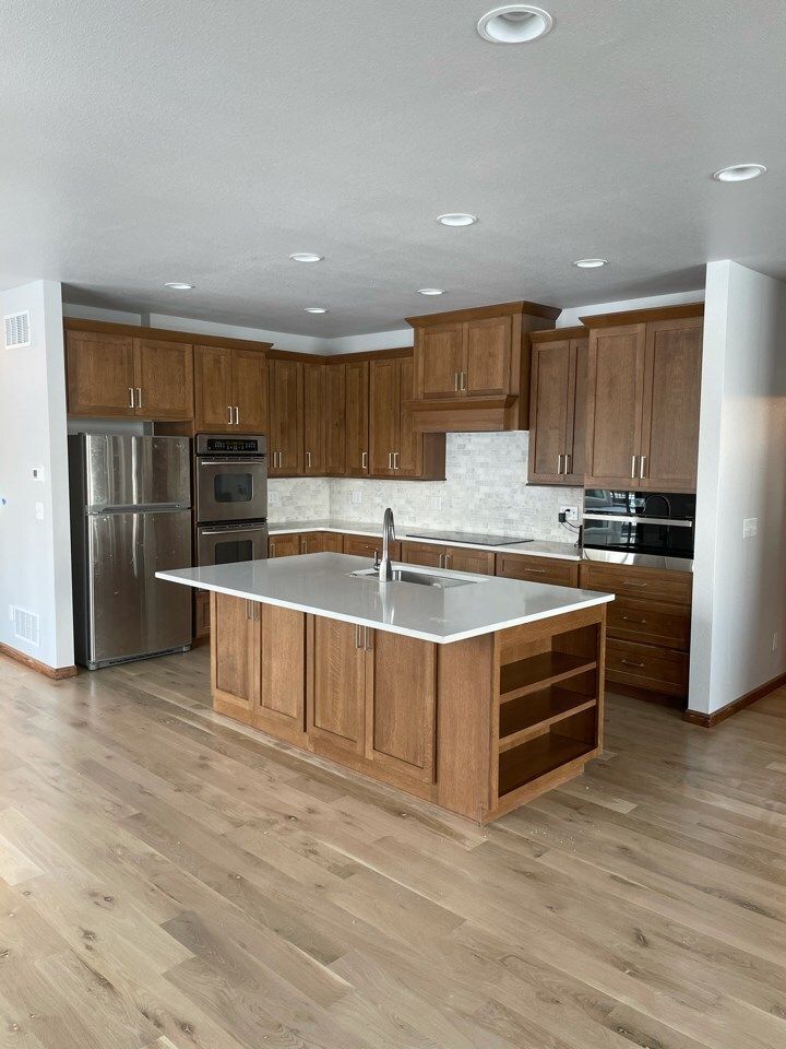 Modern kitchen with wood cabinets, stainless steel appliances, and an island. Light wood floors.