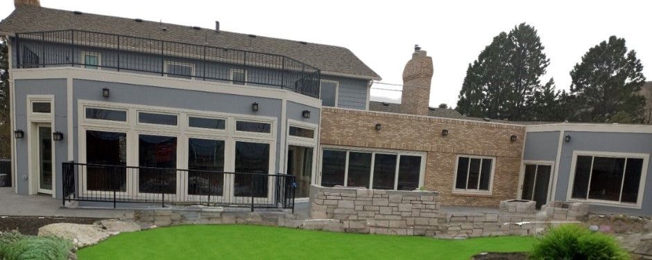 A large house with grey and stone walls, large windows, and a green lawn.