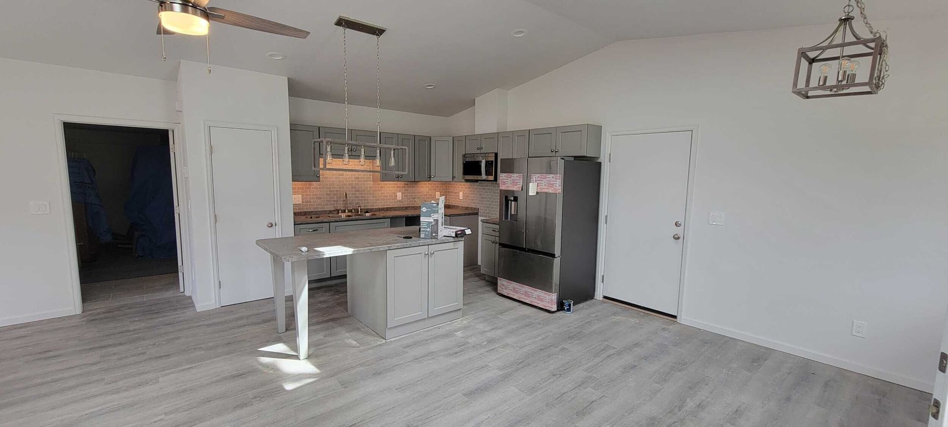 Kitchen with gray cabinets, island, stainless steel refrigerator, and light gray flooring.