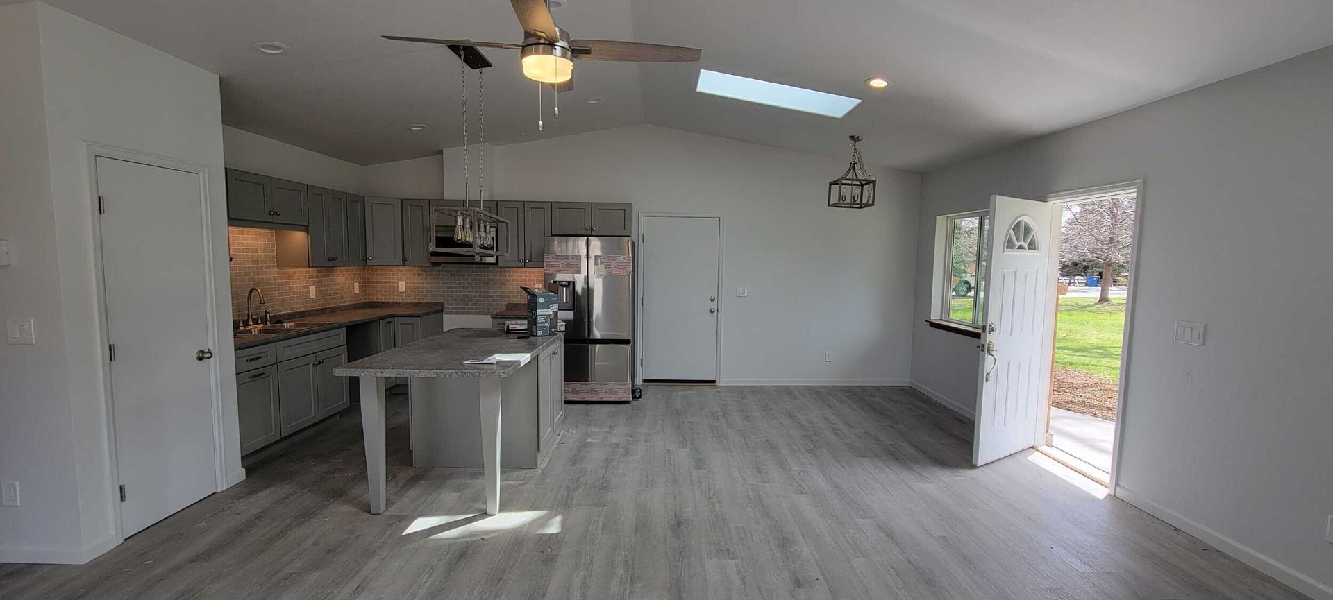 A light-filled kitchen with gray cabinets, a center island, and an open doorway to the outside.
