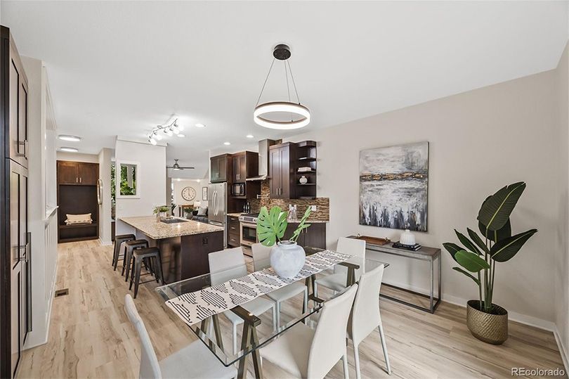 Dining room with glass table, white chairs, dark wood cabinets, and a modern light fixture.