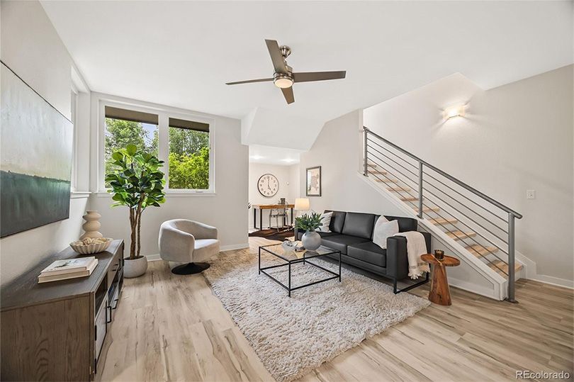 Modern living room with stairs, black couch, rug, and natural light.