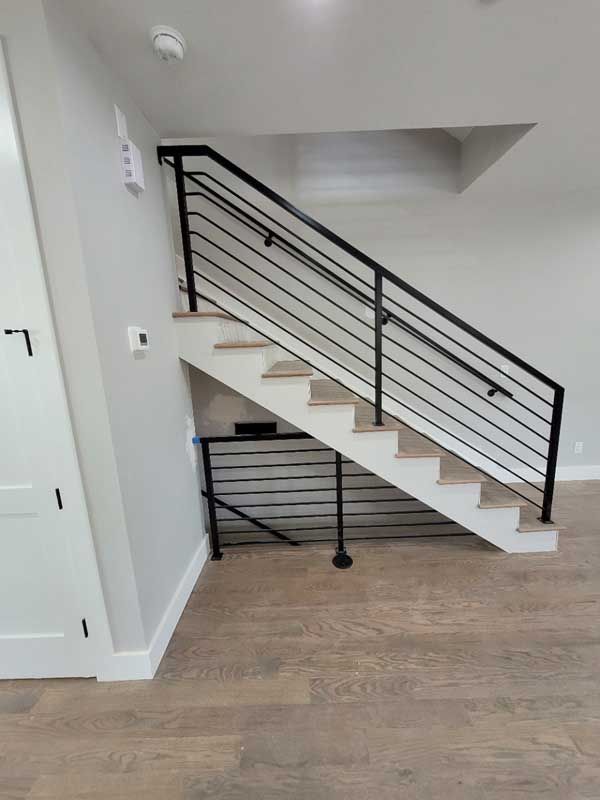 Modern black metal railing on a staircase with light wooden steps, in a home with light-colored walls and flooring.