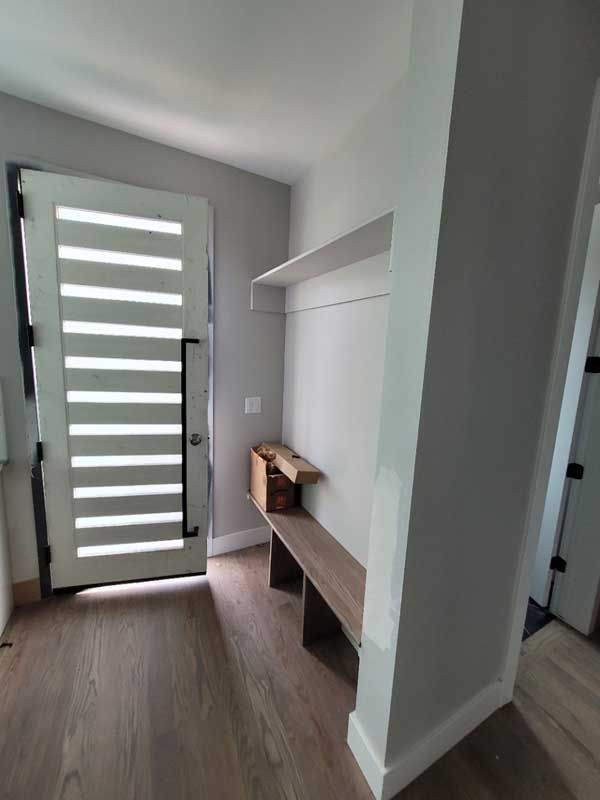 Entryway with a white door, built-in bench, and light wood flooring. The walls are gray.
