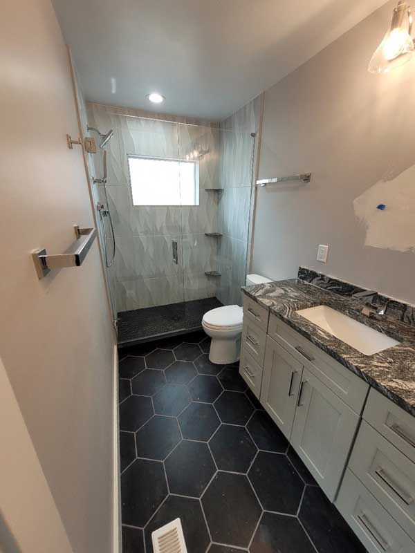 Modern bathroom with gray walls, hexagon black floor tiles, walk-in shower, white vanity, and toilet.