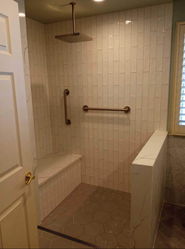 Accessible bathroom with tiled walls, built-in bench, grab bars, and a rain showerhead.