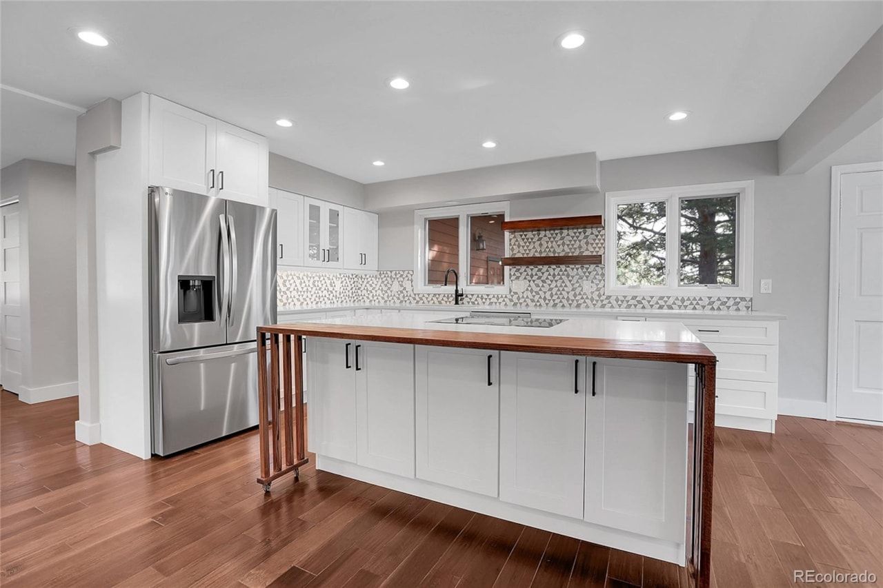 Modern white kitchen with stainless steel appliances, wooden island, and hardwood floors.