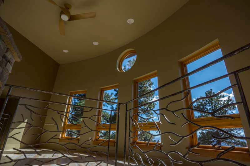 Interior view of a home with curved walls, windows, and a decorative metal railing overlooking a mountain view.