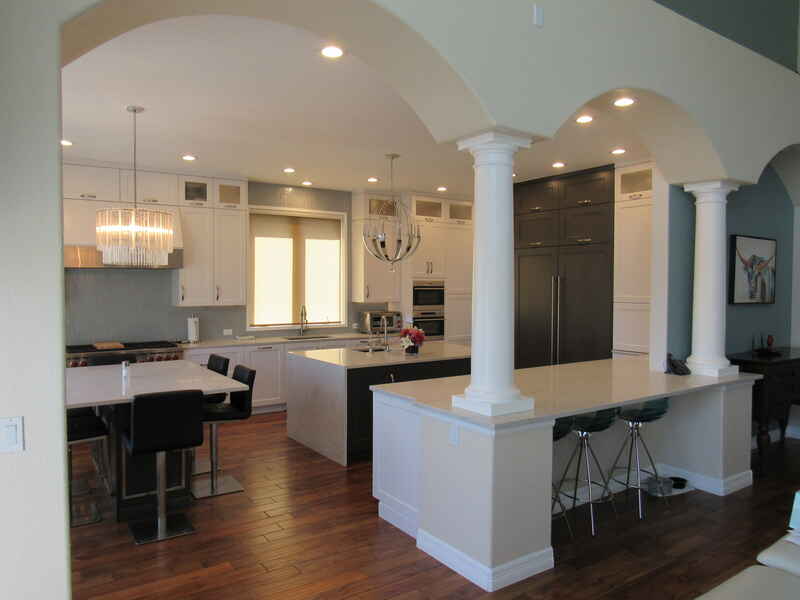 Spacious kitchen with white cabinets, dark island, columns, dining table, and wood floors.