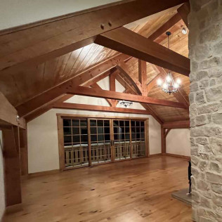 Wooden beamed ceiling with a windowed wall and hardwood floors, light-filled interior.