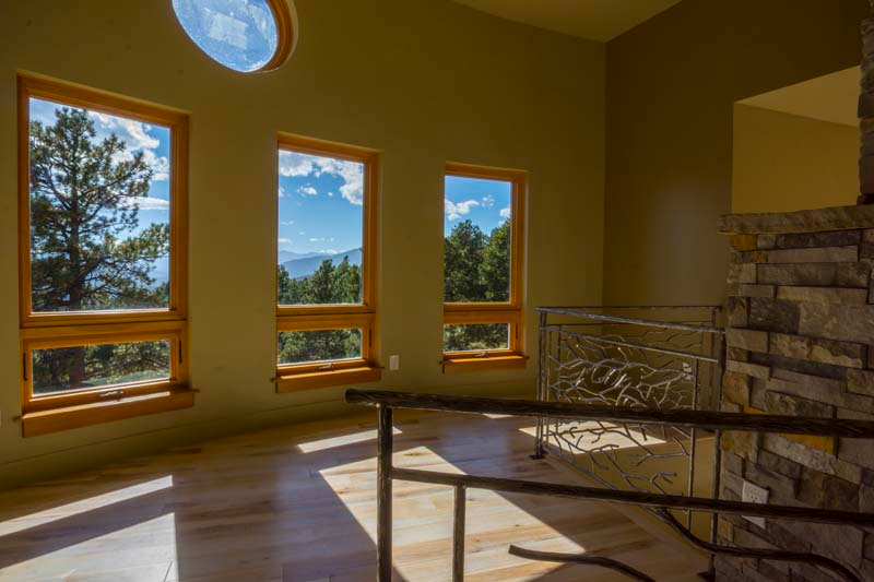 Interior room with wooden windows framing a view of trees, mountains, and blue sky.