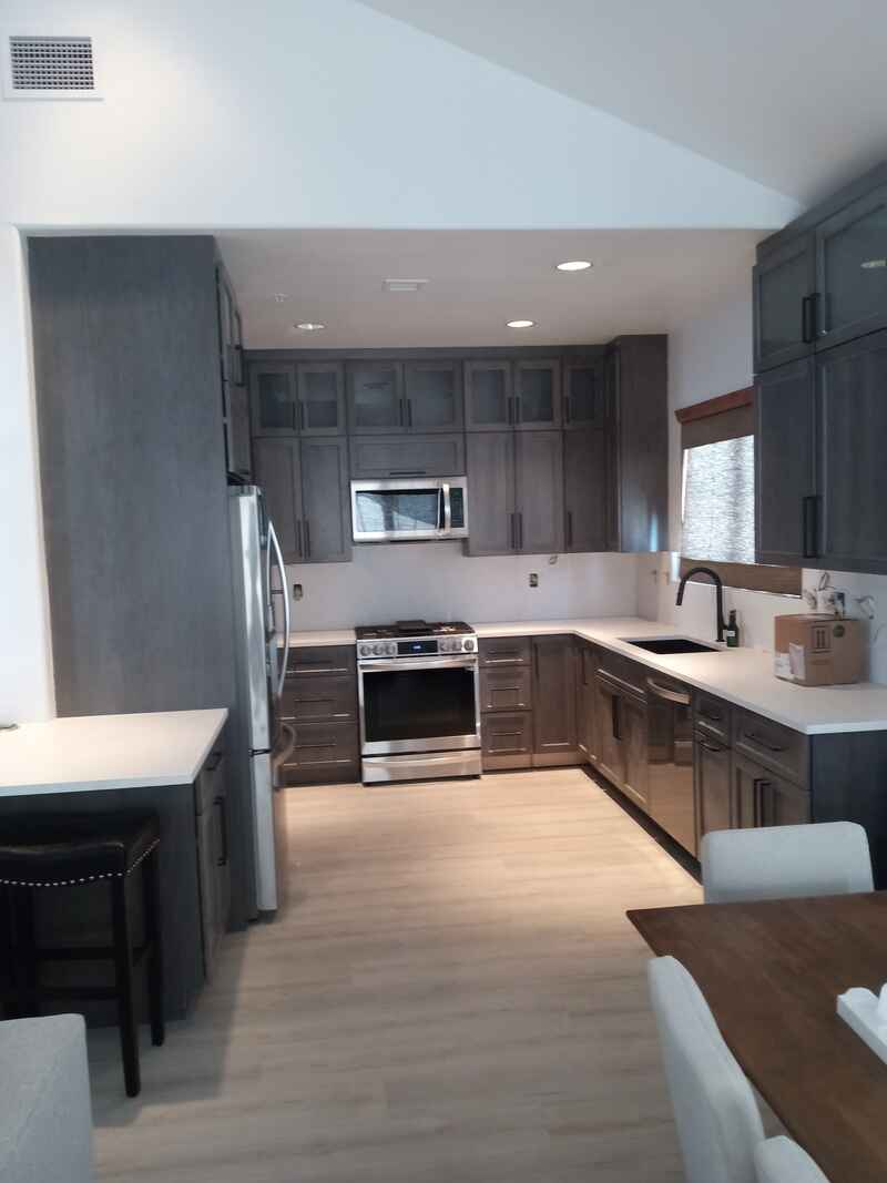 Modern kitchen with gray cabinets, stainless steel appliances, and white countertops.