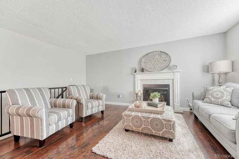 Living room with gray walls, fireplace, striped armchairs, and ottoman on a rug.
