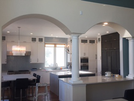Open-concept kitchen with white cabinetry, island, and columns; features a dining area with black chairs.