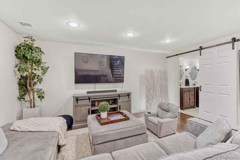 Living room with a gray sectional, TV on a wooden console, and a sliding barn door to the bathroom.