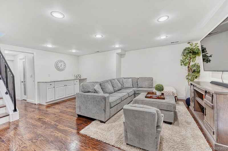 Cozy living room with gray sectional, wooden floor, white walls, TV, and a large rug.