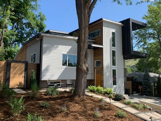 Modern house exterior with white siding, wood accents, and a black cantilevered structure.