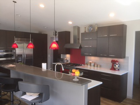 Modern kitchen with dark cabinets, red pendant lights, stainless steel appliances, and a breakfast bar.