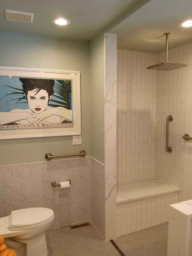 Accessible bathroom with artwork, shower bench, and grab bars; white and blue tones.