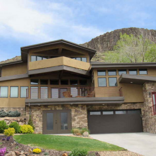 Two-story house with stone facade, brown garage door and balcony, set against a mountain.