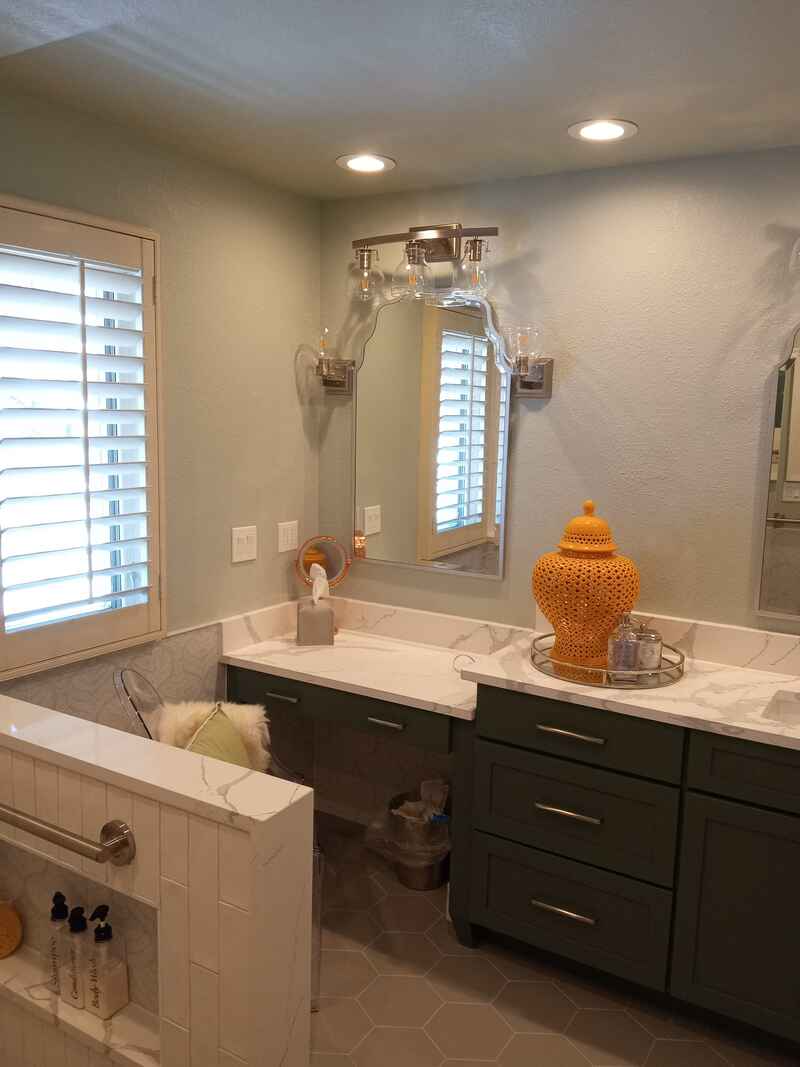 Bathroom with green cabinets, white countertops, and a large window with shutters.