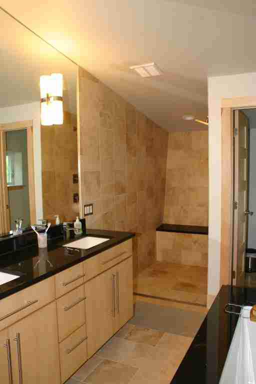 Modern bathroom with light wood vanity, black countertop, stone shower, and large mirror.
