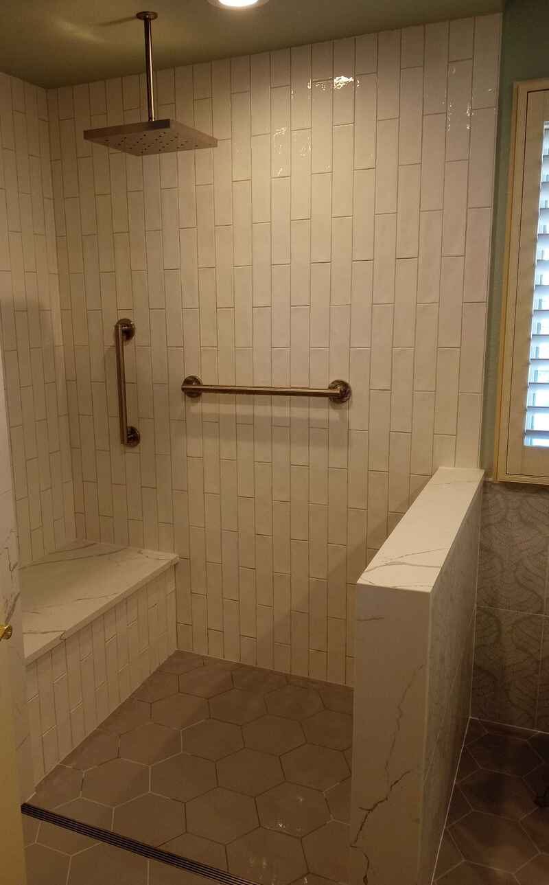Accessible shower with bench seat, grab bars, and textured white tiles.