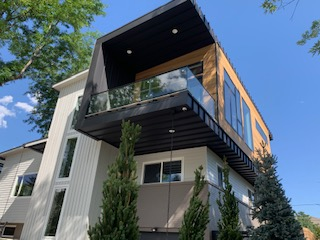 Modern two-story house with cantilevered black and wood-toned balcony, clear glass railings, and large windows.